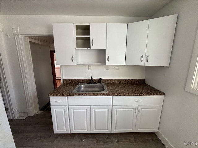 kitchen featuring dark countertops, open shelves, dark wood finished floors, white cabinetry, and a sink