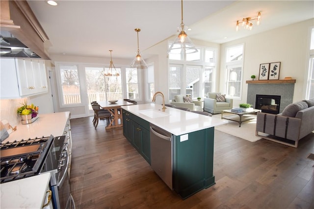 kitchen featuring dark wood finished floors, light countertops, appliances with stainless steel finishes, a glass covered fireplace, and a sink