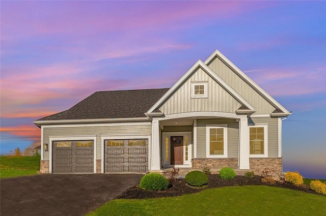 craftsman inspired home with driveway, an attached garage, a yard, stone siding, and board and batten siding