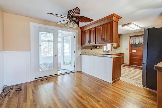 kitchen with ceiling fan, wainscoting, a peninsula, freestanding refrigerator, and light wood-style floors