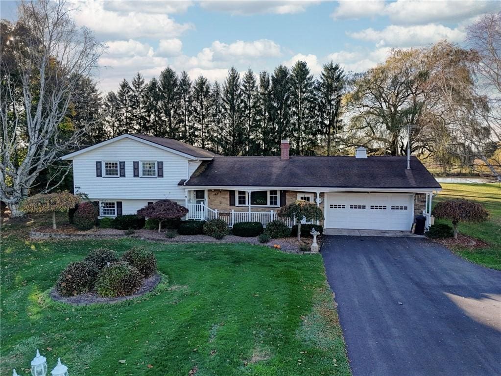 tri-level home featuring a front lawn, driveway, covered porch, a garage, and a chimney