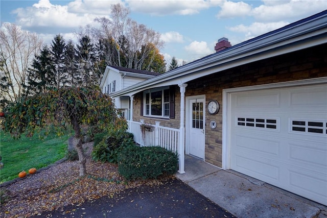 entrance to property with stone siding, a porch, a chimney, and a garage