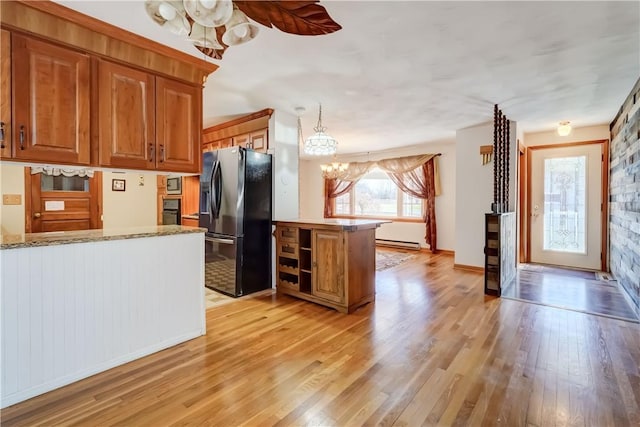 kitchen with light wood-type flooring, a peninsula, brown cabinets, baseboard heating, and black refrigerator with ice dispenser