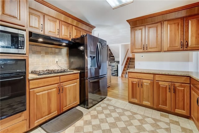 kitchen featuring under cabinet range hood, light stone counters, light floors, and appliances with stainless steel finishes