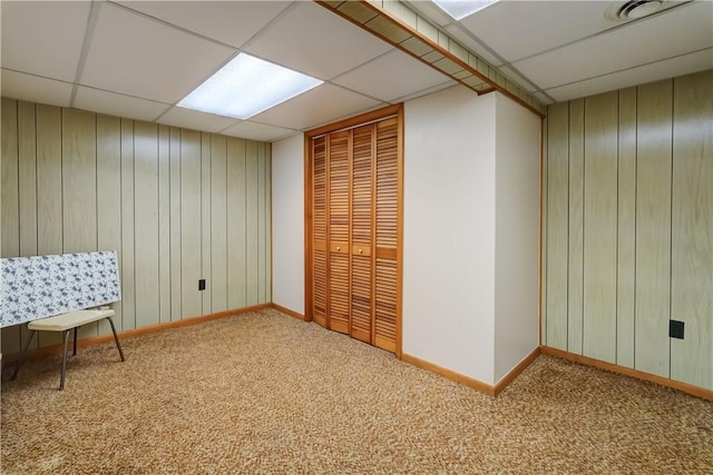 interior space with a drop ceiling, wood walls, baseboards, and carpet floors