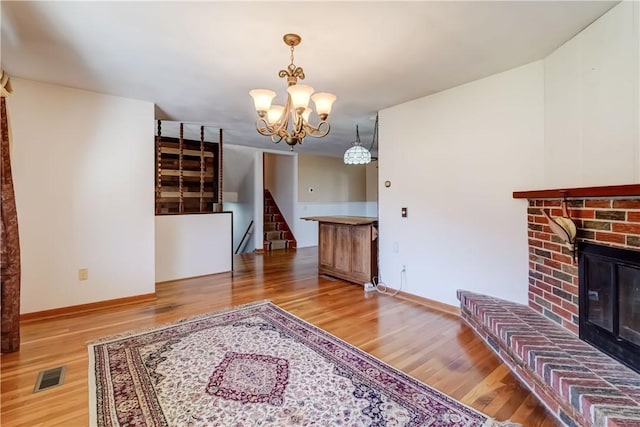 living area featuring baseboards, visible vents, light wood-style flooring, a fireplace, and a chandelier