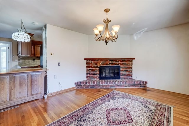 unfurnished living room with visible vents, a notable chandelier, a brick fireplace, and wood finished floors