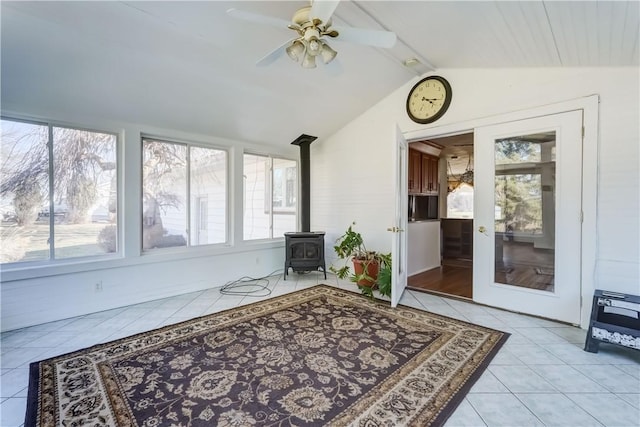 sunroom with a wealth of natural light, a wood stove, a ceiling fan, and vaulted ceiling