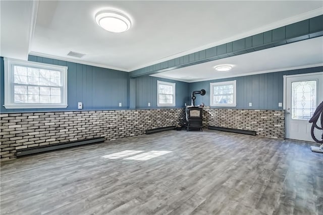 interior space with wood finished floors, brick wall, a wood stove, ornamental molding, and a baseboard heating unit