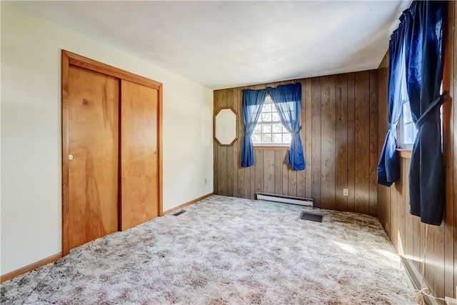 unfurnished bedroom with a closet, carpet floors, wood walls, and a baseboard radiator