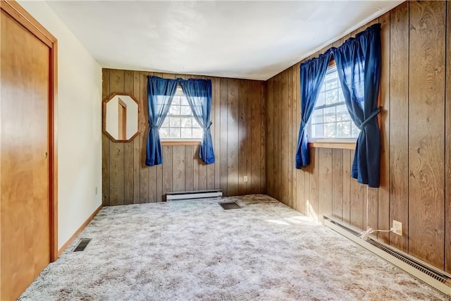 carpeted empty room featuring a baseboard heating unit, wooden walls, visible vents, and a baseboard radiator