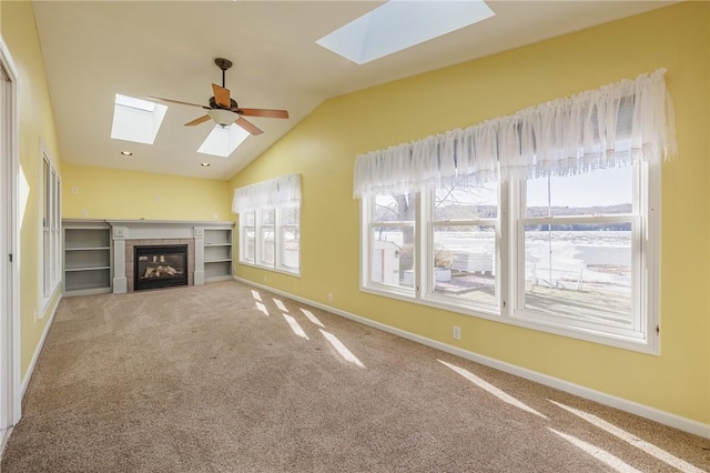 unfurnished living room with a tiled fireplace, lofted ceiling with skylight, baseboards, and carpet floors