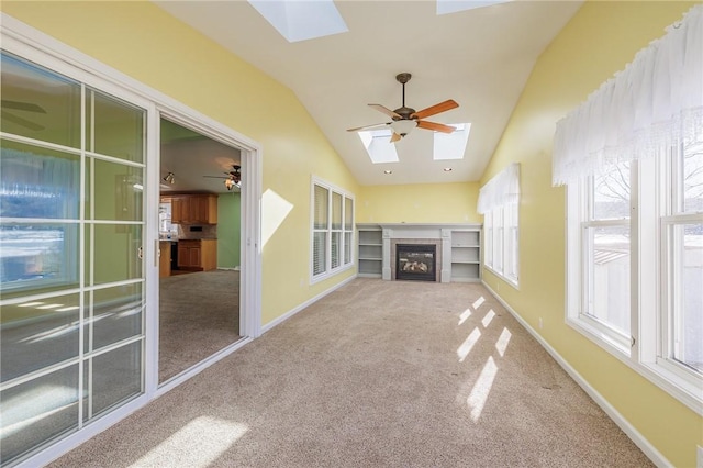 unfurnished sunroom featuring a glass covered fireplace, vaulted ceiling with skylight, and ceiling fan