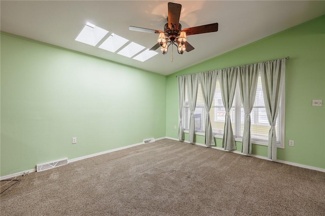 carpeted empty room with visible vents, vaulted ceiling with skylight, baseboards, and a ceiling fan