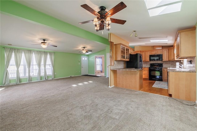 kitchen featuring vaulted ceiling with skylight, decorative backsplash, black appliances, light carpet, and open floor plan