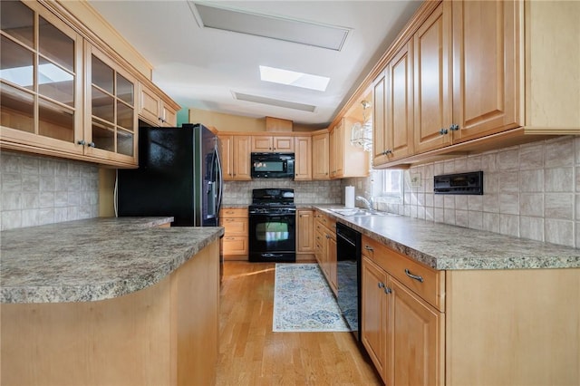 kitchen featuring black appliances, light wood-style flooring, a sink, tasteful backsplash, and vaulted ceiling with skylight