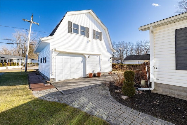 view of side of home featuring a gambrel roof, an attached garage, a lawn, and decorative driveway