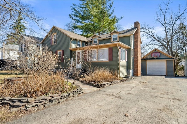 view of front of home with a detached garage, driveway, an outdoor structure, and a chimney