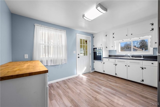 kitchen featuring light wood-type flooring, a sink, white cabinetry, stainless steel oven, and baseboards