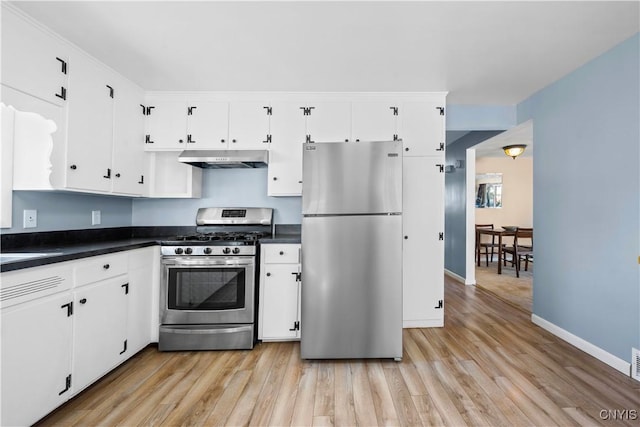 kitchen with dark countertops, under cabinet range hood, light wood-style flooring, appliances with stainless steel finishes, and white cabinetry