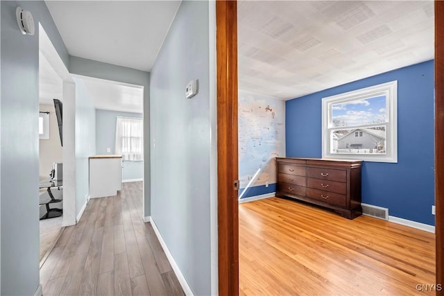 hallway featuring visible vents, light wood-style flooring, and baseboards