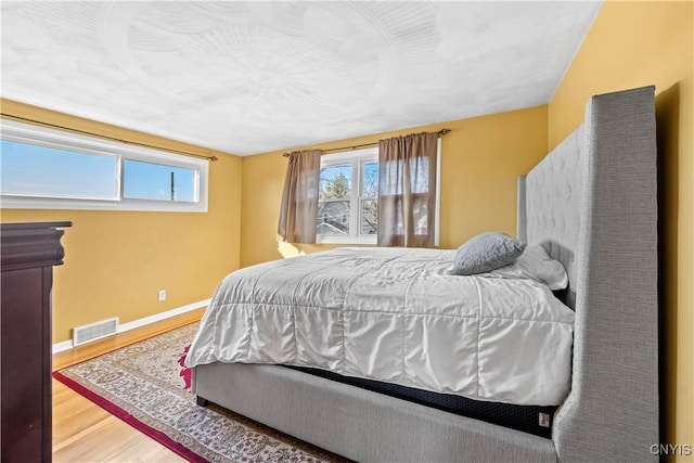 bedroom featuring visible vents, multiple windows, baseboards, and wood finished floors