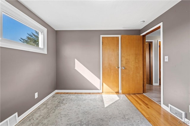 unfurnished bedroom with visible vents, baseboards, a closet, and wood finished floors