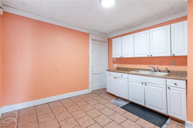 kitchen with a sink, baseboards, light tile patterned floors, and white cabinetry