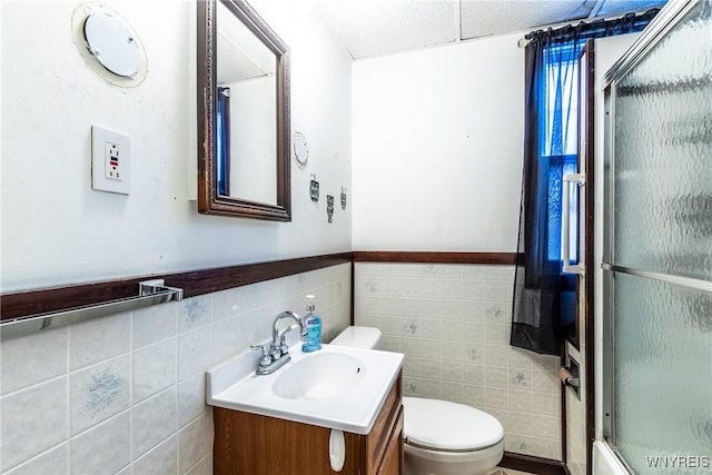 bathroom with vanity, tile walls, toilet, and a shower with door