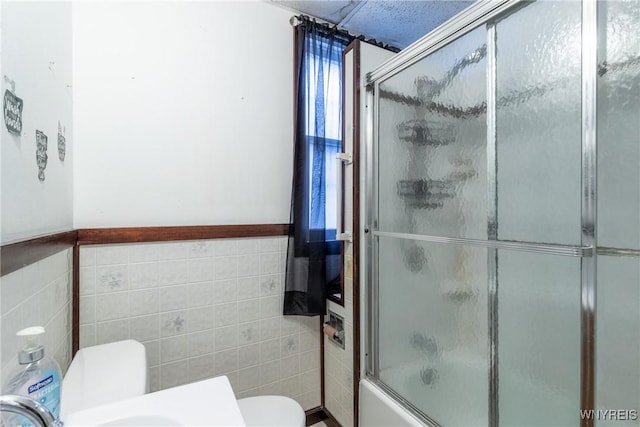 bathroom with toilet, tile walls, and shower / bath combination with glass door