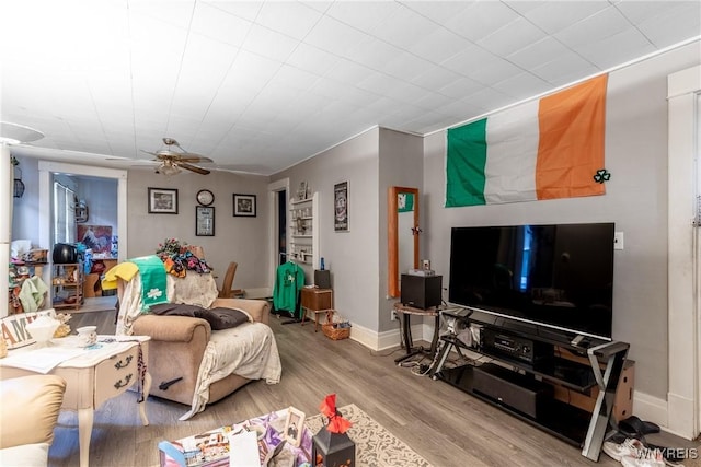 living area with baseboards, wood finished floors, and a ceiling fan