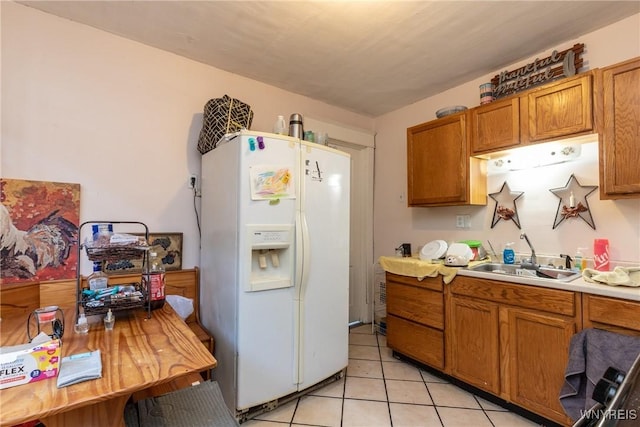 kitchen featuring light countertops, light tile patterned floors, brown cabinets, white refrigerator with ice dispenser, and a sink