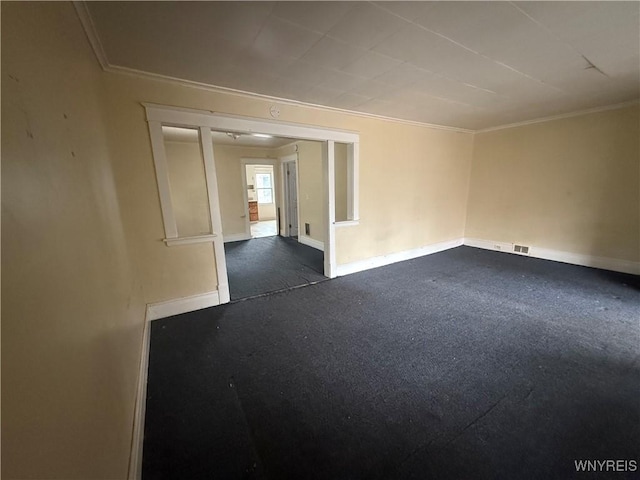 empty room featuring visible vents, dark carpet, baseboards, and ornamental molding