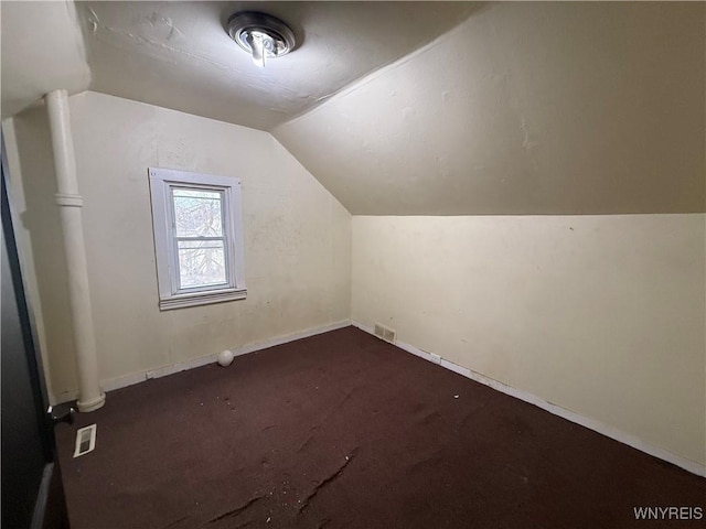 additional living space with dark colored carpet, visible vents, baseboards, and vaulted ceiling