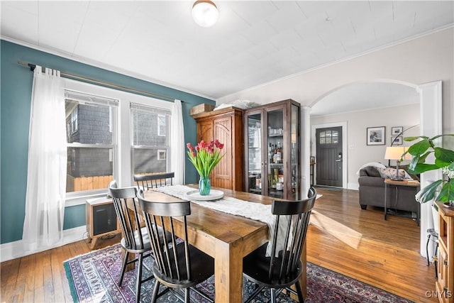 dining space featuring arched walkways, ornamental molding, baseboards, and hardwood / wood-style flooring