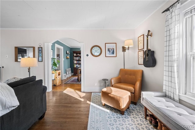 living room featuring arched walkways, dark wood-style floors, baseboards, and ornamental molding