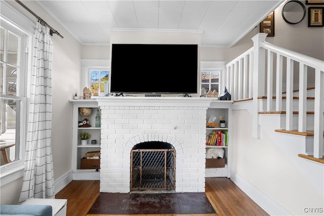 living area featuring baseboards, wood finished floors, a fireplace, and crown molding