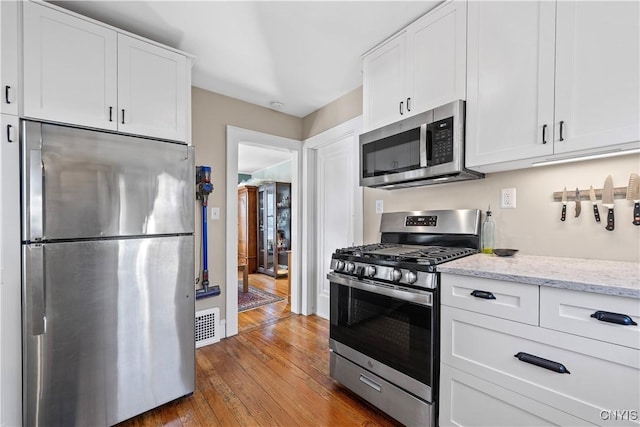 kitchen featuring visible vents, hardwood / wood-style flooring, light stone counters, stainless steel appliances, and white cabinets