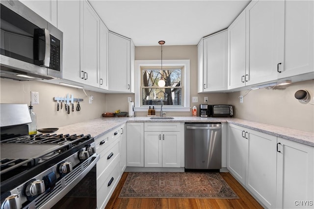 kitchen with light stone countertops, dark wood-style floors, a sink, stainless steel appliances, and white cabinetry