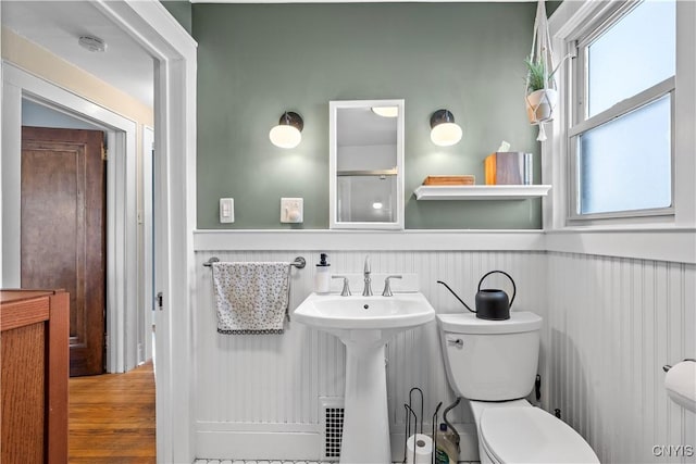 bathroom featuring wood finished floors, wainscoting, a sink, walk in shower, and toilet