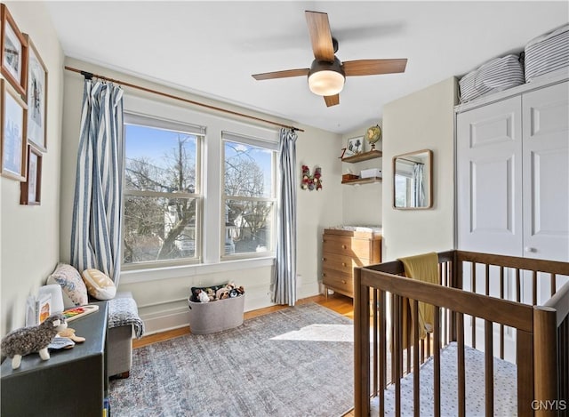 bedroom with a closet, a ceiling fan, a nursery area, and wood finished floors