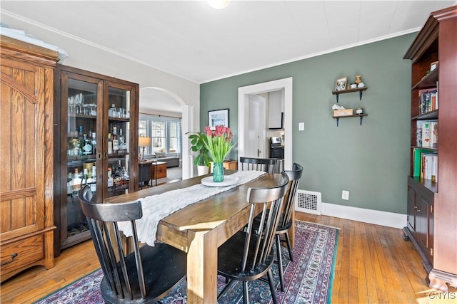 dining space featuring visible vents, crown molding, baseboards, arched walkways, and wood-type flooring