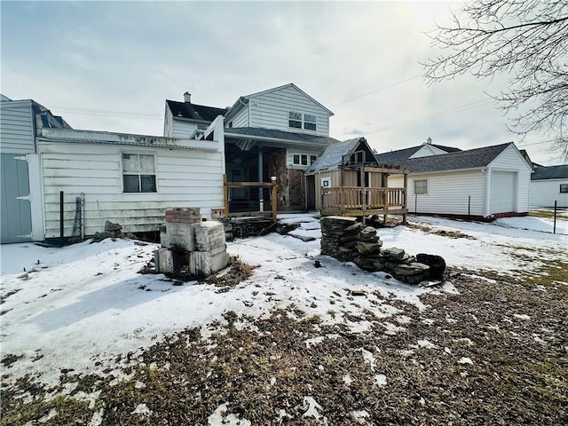 snow covered rear of property with a garage and a wooden deck