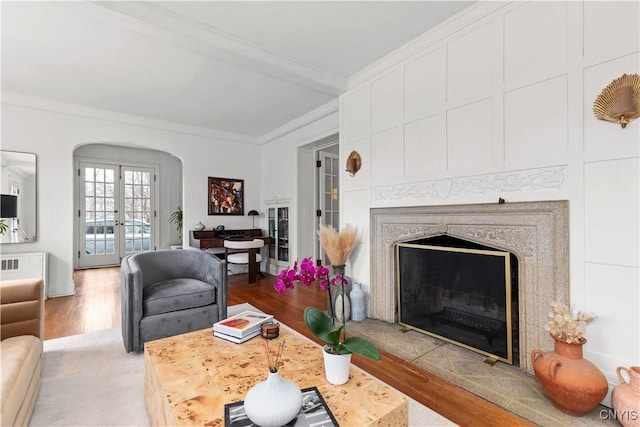 living area with a high end fireplace, crown molding, french doors, wood finished floors, and arched walkways