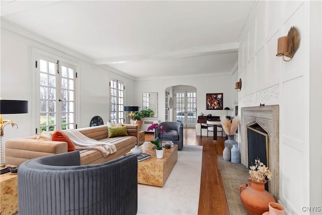 living area featuring a premium fireplace, light wood-style flooring, arched walkways, french doors, and crown molding