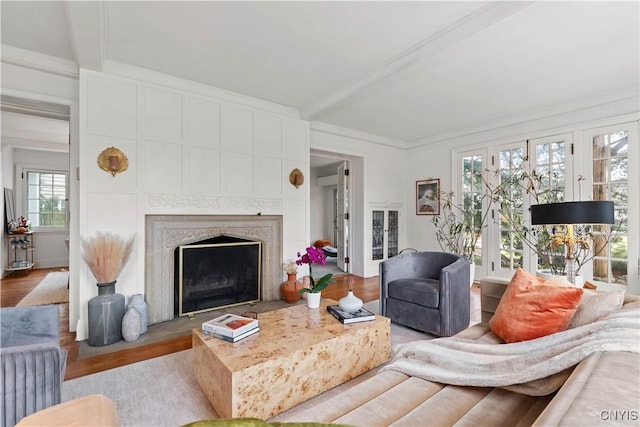 living room featuring beamed ceiling, wood finished floors, a high end fireplace, and ornamental molding