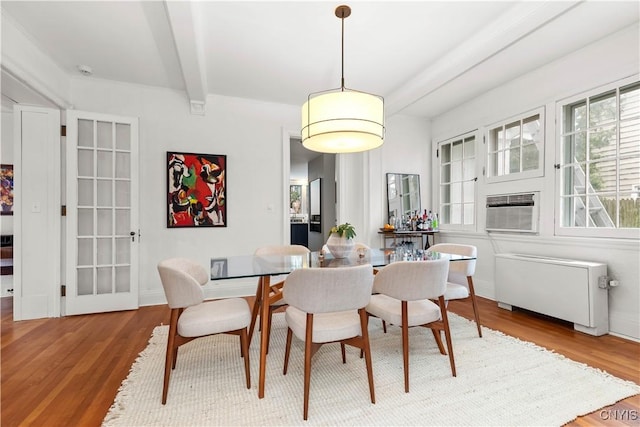 dining area featuring beam ceiling, cooling unit, radiator, and wood finished floors