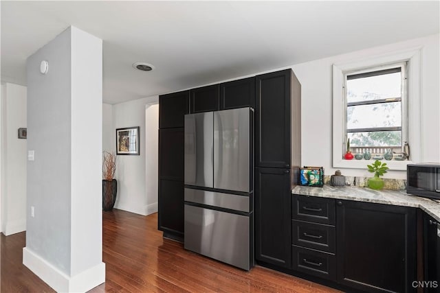 kitchen featuring wood finished floors, freestanding refrigerator, black microwave, and dark cabinets