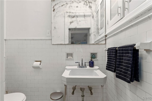 bathroom featuring toilet, tile walls, and a sink