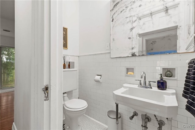 bathroom featuring toilet, wainscoting, tile patterned floors, tile walls, and a sink